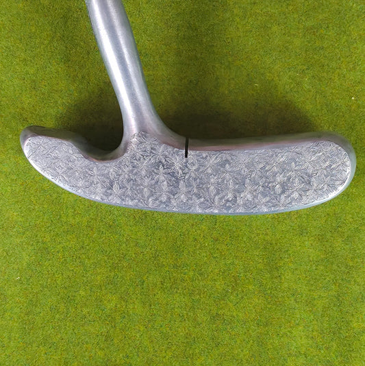 Close-up of a golf putter head on a green surface