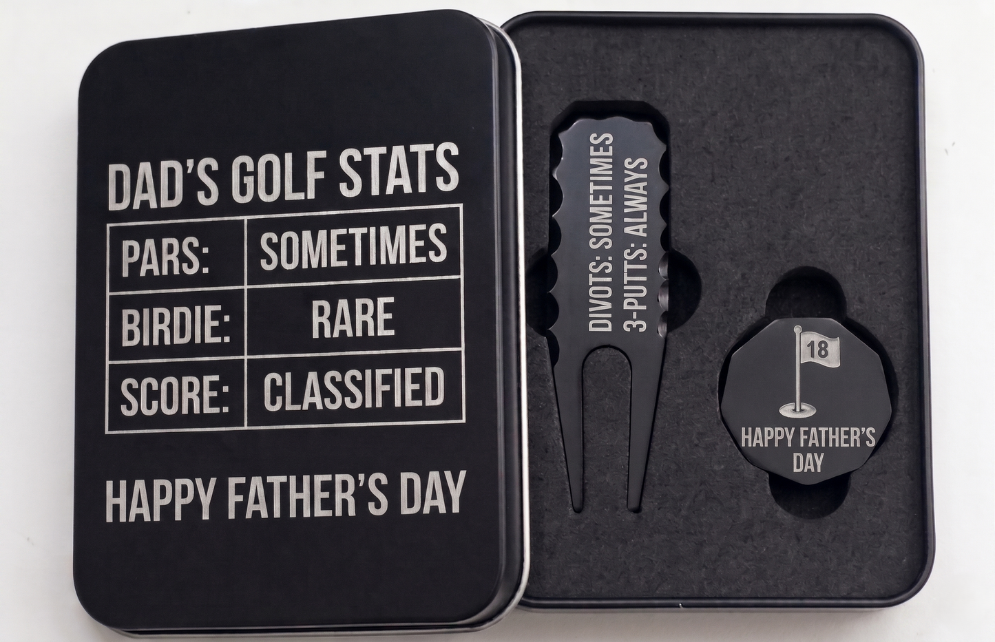 Black metal golf gift set for Father's Day in a custom engraved tin box. Inside sits a customized divot repair tool and a round ball marker resting in foam. Engraving options include sentimental quotes from kids, funny dad golf stats like three-putts, topographic patterns with initials, or classic crossed golf clubs. A perfect personalized fathers or grandpa gift for the golf course. The dark matte metal provides high contrast for the silver laser engraving, making the text pop nicely.
