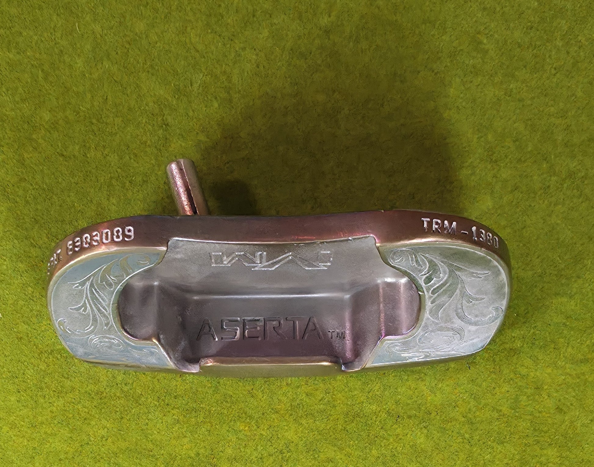 Custom engraved golf putter head with ornate floral and scrollwork design in antique brushed metal finish. Features deep engraving for durability, luxury artisan detailing, and an elegant symmetrical pattern. Perfect for golfers seeking a unique club, golf collectors, or as a personalized gift with initials, logos, or dates added. A blend of performance and craftsmanship designed to stand out on the green or in a golf display collection.
