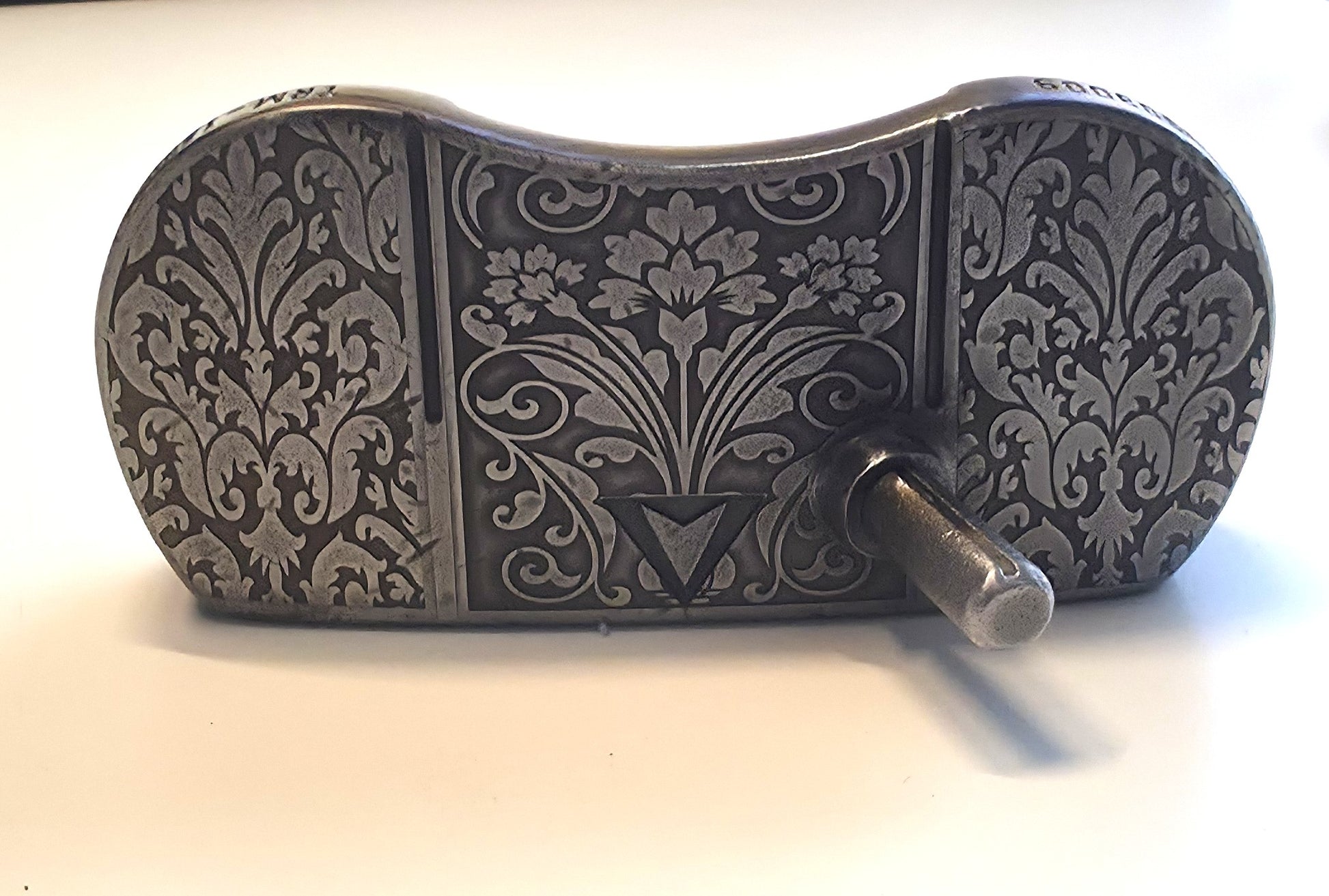 Decorative metal object with intricate patterns on a white background Custom engraved golf putter head with ornate floral and scrollwork design in antique brushed metal finish. Features deep engraving for durability, luxury artisan detailing, and an elegant symmetrical pattern. Perfect for golfers seeking a unique club, golf collectors, or as a personalized gift with initials, logos, or dates added. A blend of performance and craftsmanship designed to stand out on the green or in a golf display collection.