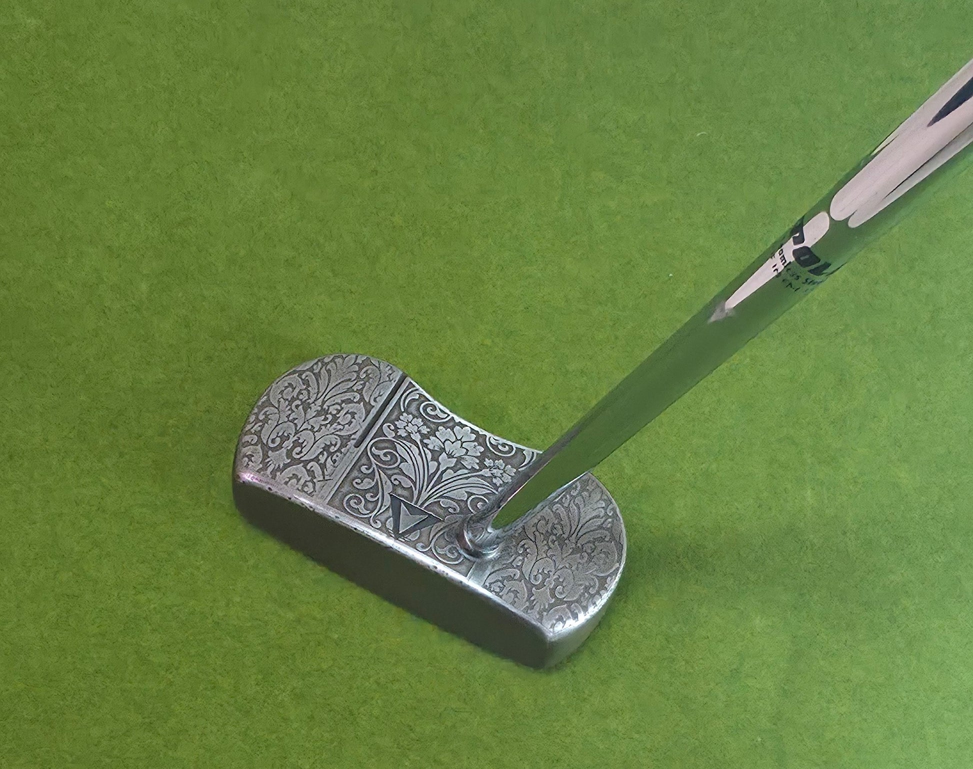 Custom engraved golf putter head with ornate floral and scrollwork design in antique brushed metal finish. Features deep engraving for durability, luxury artisan detailing, and an elegant symmetrical pattern. Perfect for golfers seeking a unique club, golf collectors, or as a personalized gift with initials, logos, or dates added. A blend of performance and craftsmanship designed to stand out on the green or in a golf display collection.