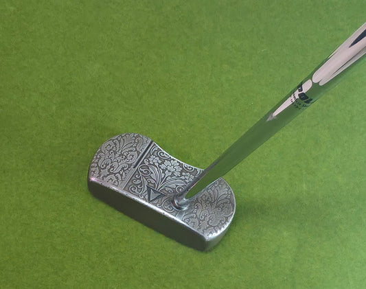 Custom engraved golf putter head with ornate floral and scrollwork design in antique brushed metal finish. Features deep engraving for durability, luxury artisan detailing, and an elegant symmetrical pattern. Perfect for golfers seeking a unique club, golf collectors, or as a personalized gift with initials, logos, or dates added. A blend of performance and craftsmanship designed to stand out on the green or in a golf display collection.