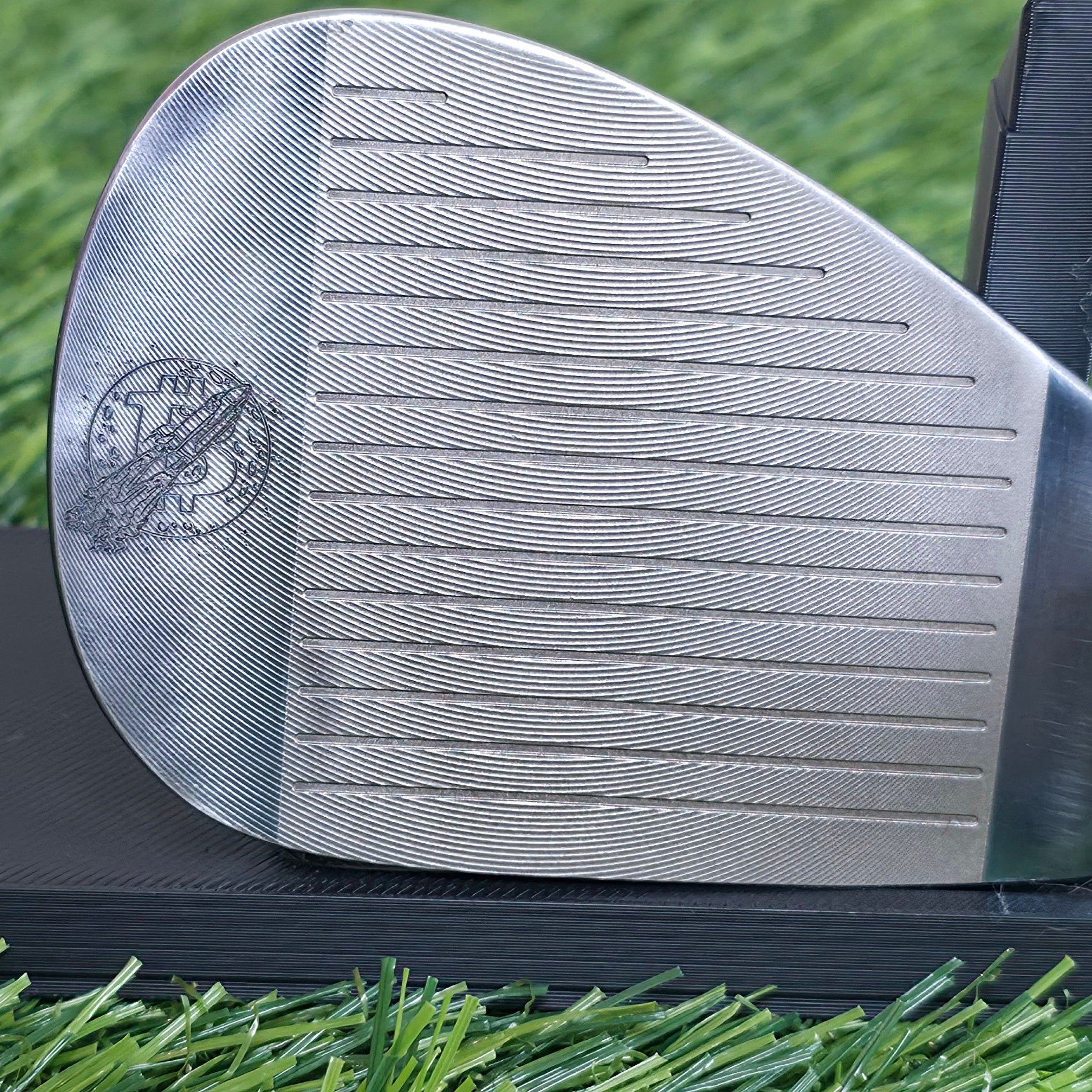 A 60-degree golf lob wedge featuring a custom laser-engraved Bitcoin theme. The back of the metal clubhead displays a central Bitcoin logo surrounded by a complex network of smaller Bitcoin icons and interconnected blockchain nodes. The club face features standard scoring grooves with a detailed engraving of a Bitcoin rocket ship on the toe. Resting on vibrant green artificial turf, this unique wedge seamlessly combines modern cryptocurrency culture with premium custom golf equipment design.