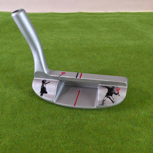 A silver metal golf putter with graffiti-style black and red illustrations, resting on a green artificial turf background. Silver golf chipper on green turf. Back features black and red laser-engraved street art silhouettes: a girl reaching for a red heart balloon, and a man throwing red flowers. Top line has a red heart and black/red alignment stripes. The front face shows standard horizontal scoring lines. The metal club head connects to a silver shaft at the heel. These high-contrast deep engravings are 