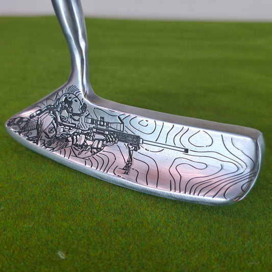 A silver metal golf putter head with black engraved topographic contour lines and a skeleton holding a rifle, resting on a green grass surface.A silver Dunlop blade golf putter on green turf. The sole features a detailed, custom black laser engraving of a tactical military sniper aiming a scoped rifle on a bipod, set against winding topographical map lines. The back cavity has a black section with white Dunlop text and a target logo. The front club face includes a rectangular red insert. This custom modifie