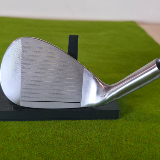 Close-up of a custom-engraved silvery 52-degree golf wedge on green grass. The club head features a deep black laser engraving of Anime Pirate tipping his straw hat.  The Pirate skull logo is etched near the top edge. This brushed steel club blends anime fandom with golf, showcasing high-contrast, permanent artwork. Perfect for display or play, it highlights crisp lines upon a brilliant metallic golf surface.