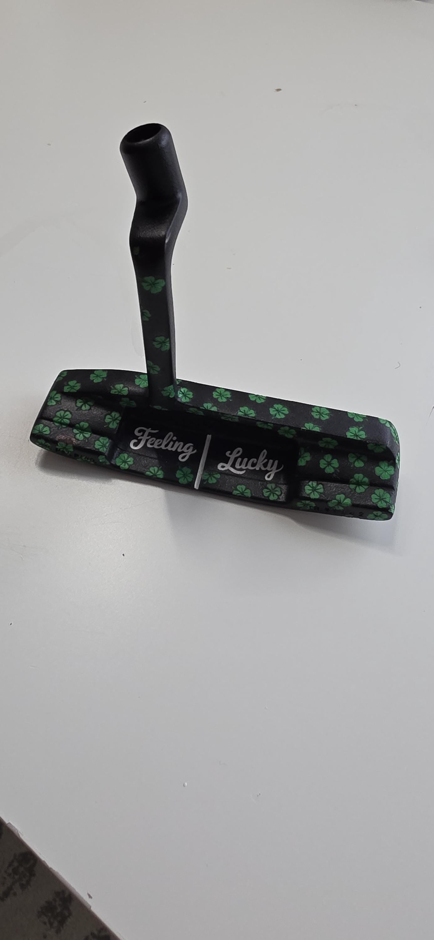 Custom black golf putter with green shamrock clover pattern, "Feeling Lucky" engraving, white alignment line, and Elite Golf Works USA branding — novelty St. Patrick’s Day golf gift for Irish golf lovers and collectors  custom golf putter  black putter head  green shamrock / clover pattern  “Feeling Lucky” engraving  alignment line  Elite Golf Works USA  St. Patrick’s Day golf gift  novelty golf club  Irish golf lovers  collectors
