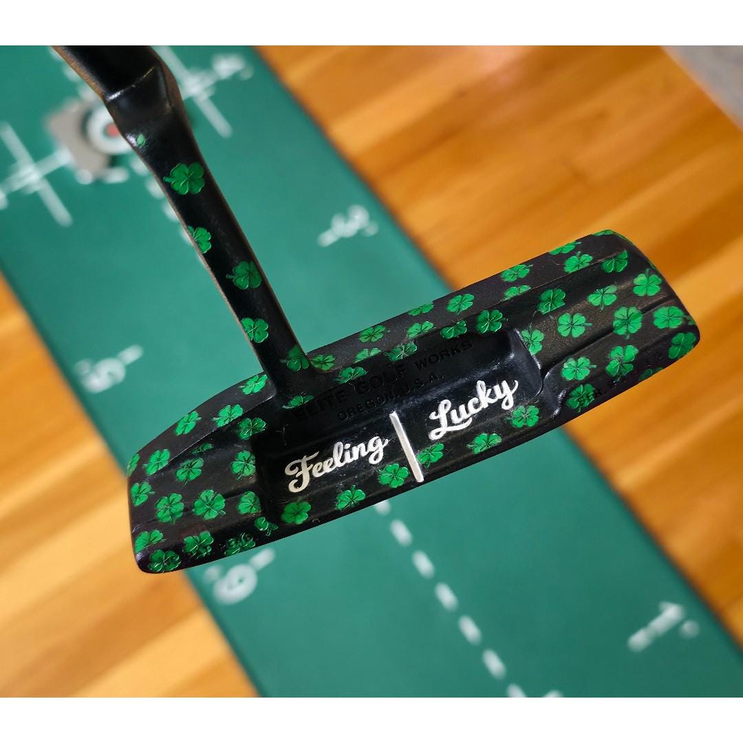 Custom black golf putter with green shamrock clover pattern, "Feeling Lucky" engraving, white alignment line, and Elite Golf Works USA branding — novelty St. Patrick’s Day golf gift for Irish golf lovers and collectors  custom golf putter  black putter head  green shamrock / clover pattern  “Feeling Lucky” engraving  alignment line  Elite Golf Works USA  St. Patrick’s Day golf gift  novelty golf club  Irish golf lovers  collectors