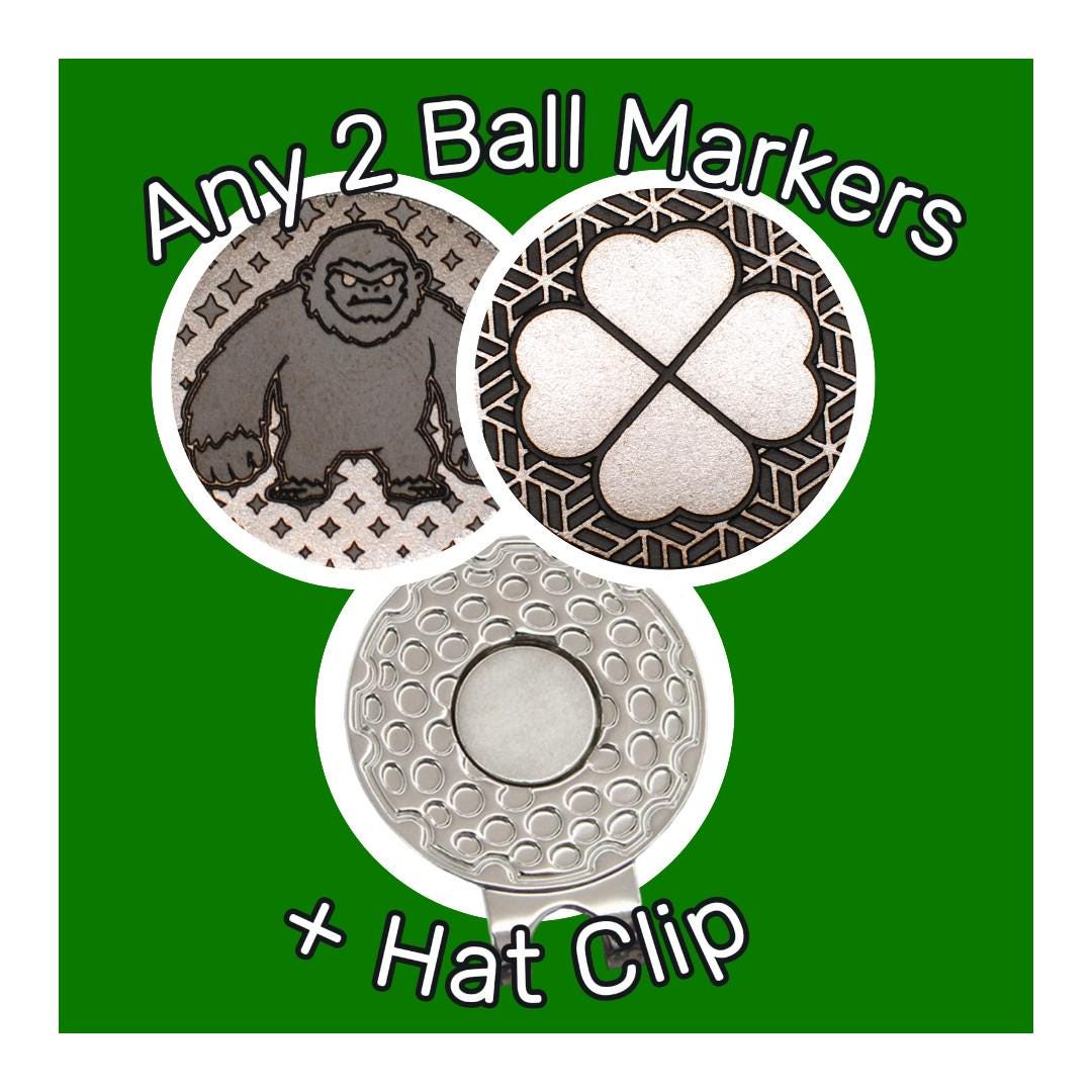 May include: Golf ball markers and hat clip set. The set includes two round markers with a gorilla and a four-leaf clover design, and a golf ball-shaped hat clip. The text "Any 2 Ball Markers + Hat Clip" is displayed.
Custom golf ball markers, Personalized golf gifts, Stainless steel,  Magnetic hat clip markers, golf accessories, Alignment ball markers, Metal golf markers, Best golf ball markers,golf accessories, magnetic golf ball markers, Unique gift for golfers, Custom engraved golf