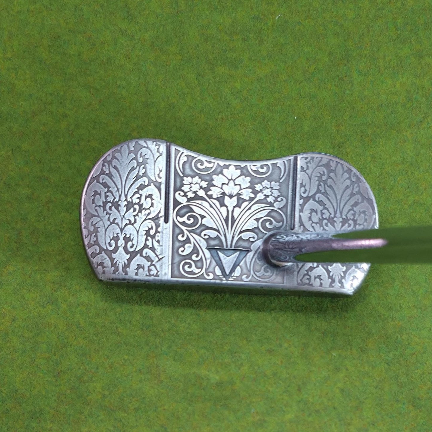 Custom engraved golf putter head with ornate floral and scrollwork design in antique brushed metal finish. Features deep engraving for durability, luxury artisan detailing, and an elegant symmetrical pattern. Perfect for golfers seeking a unique club, golf collectors, or as a personalized gift with initials, logos, or dates added. A blend of performance and craftsmanship designed to stand out on the green or in a golf display collection