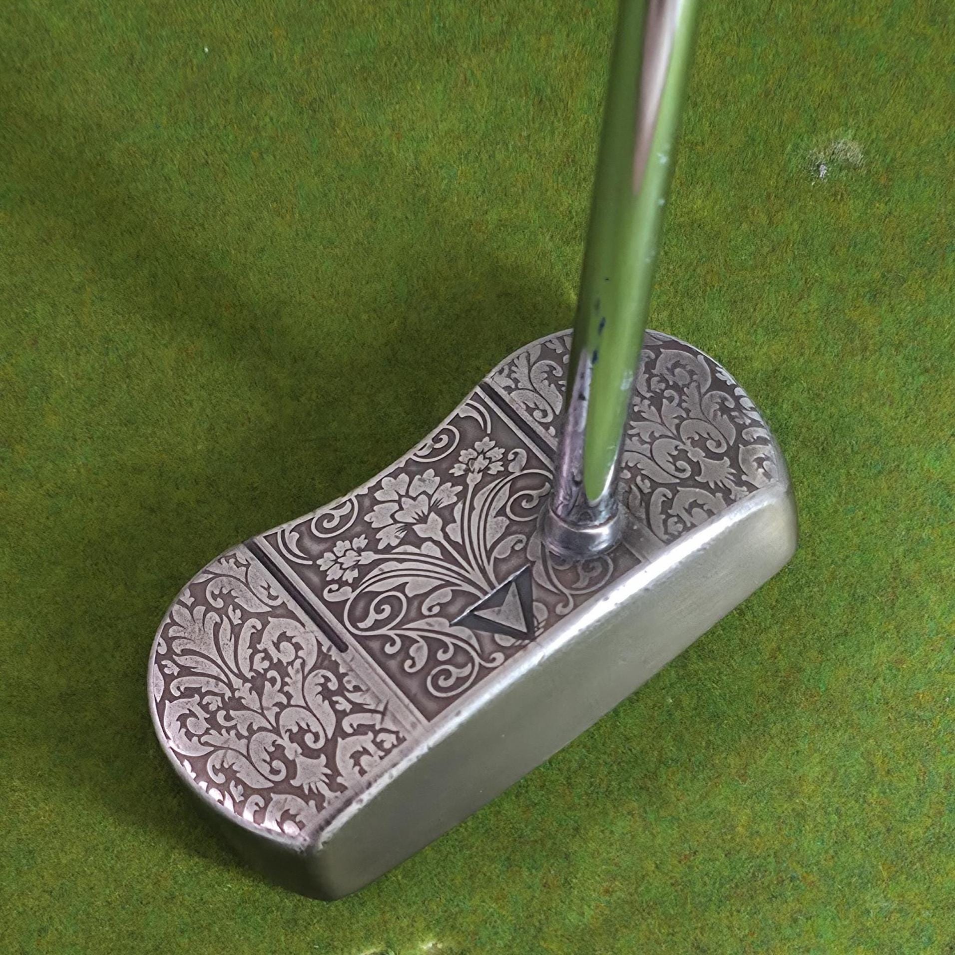 Custom engraved golf putter head with ornate floral and scrollwork design in antique brushed metal finish. Features deep engraving for durability, luxury artisan detailing, and an elegant symmetrical pattern. Perfect for golfers seeking a unique club, golf collectors, or as a personalized gift with initials, logos, or dates added. A blend of performance and craftsmanship designed to stand out on the green or in a golf display collection