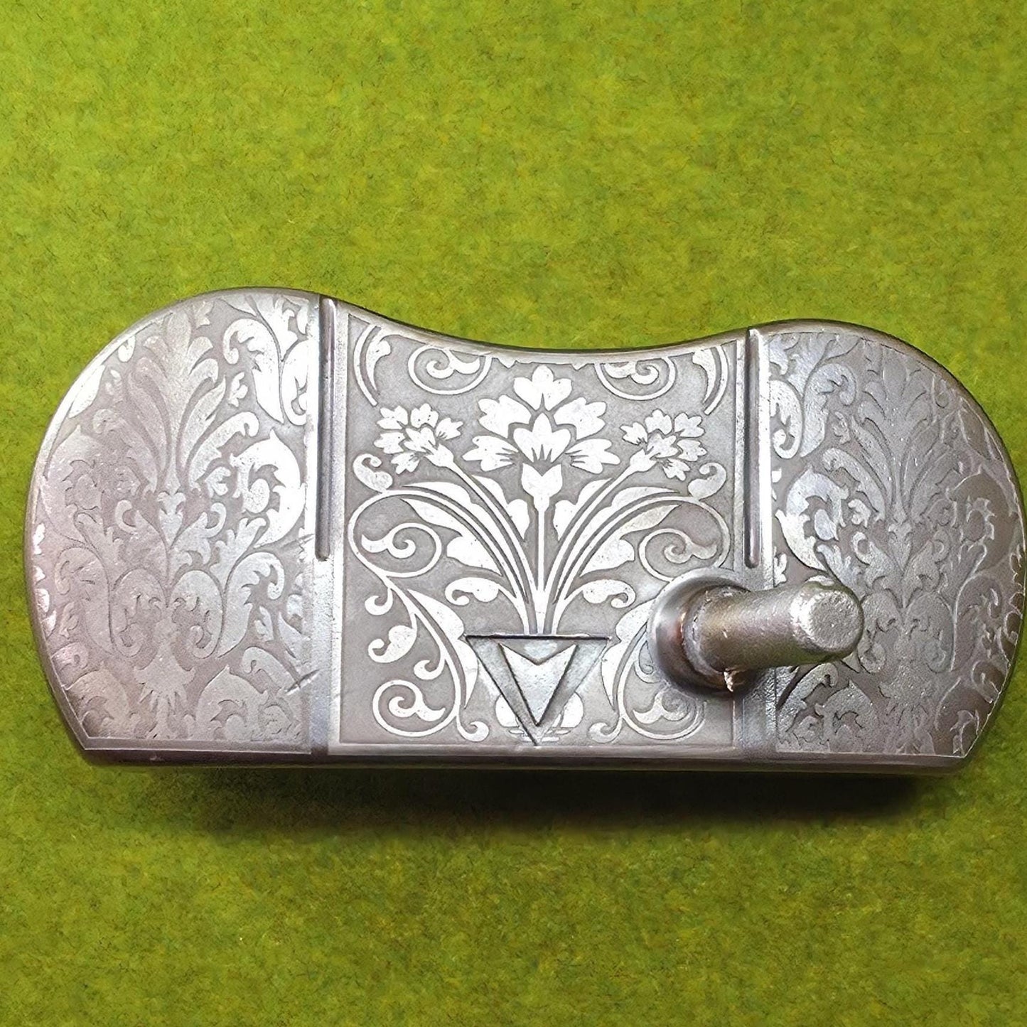 Custom engraved golf putter head with ornate floral and scrollwork design in antique brushed metal finish. Features deep engraving for durability, luxury artisan detailing, and an elegant symmetrical pattern. Perfect for golfers seeking a unique club, golf collectors, or as a personalized gift with initials, logos, or dates added. A blend of performance and craftsmanship designed to stand out on the green or in a golf display collection