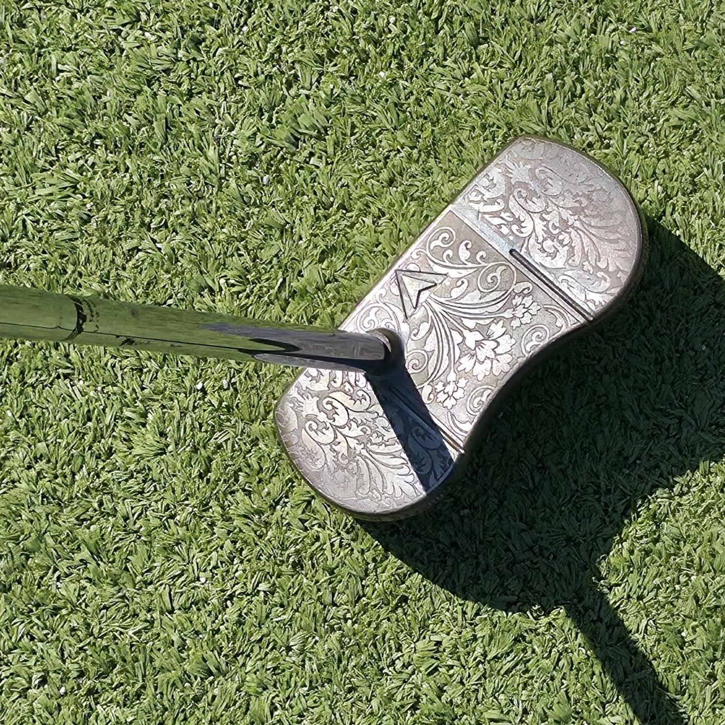 Custom engraved golf putter head with ornate floral and scrollwork design in antique brushed metal finish. Features deep engraving for durability, luxury artisan detailing, and an elegant symmetrical pattern. Perfect for golfers seeking a unique club, golf collectors, or as a personalized gift with initials, logos, or dates added. A blend of performance and craftsmanship designed to stand out on the green or in a golf display collection