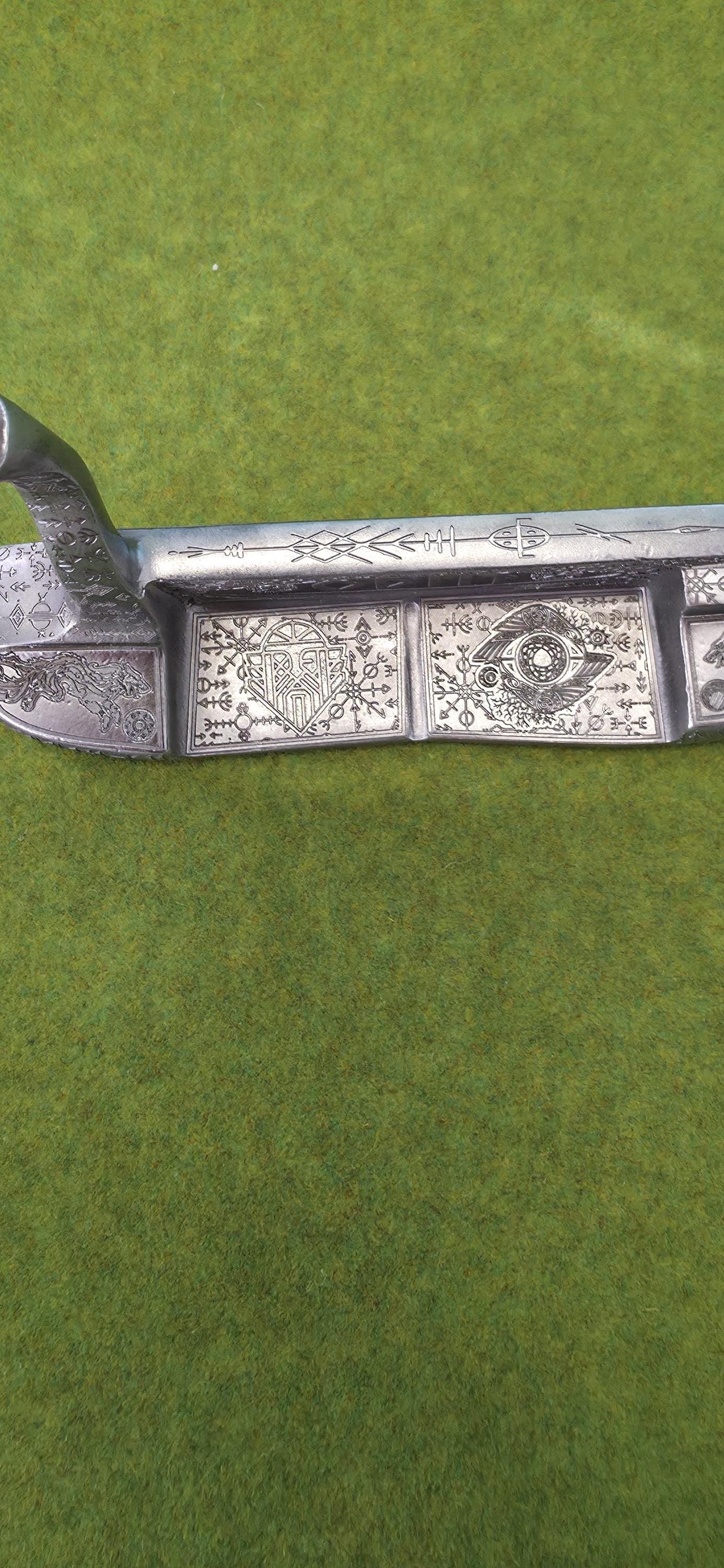 Custom hand-engraved Odin themed golf putter with Norse runes, Viking symbols, and raven designs. Features darkened engravings, raw steel finish, and detailed artwork on the face, back cavity, sole, and neck. Inspired by Norse mythology and Viking craftsmanship. Perfect for golf collectors or players who want a unique personalized putter.