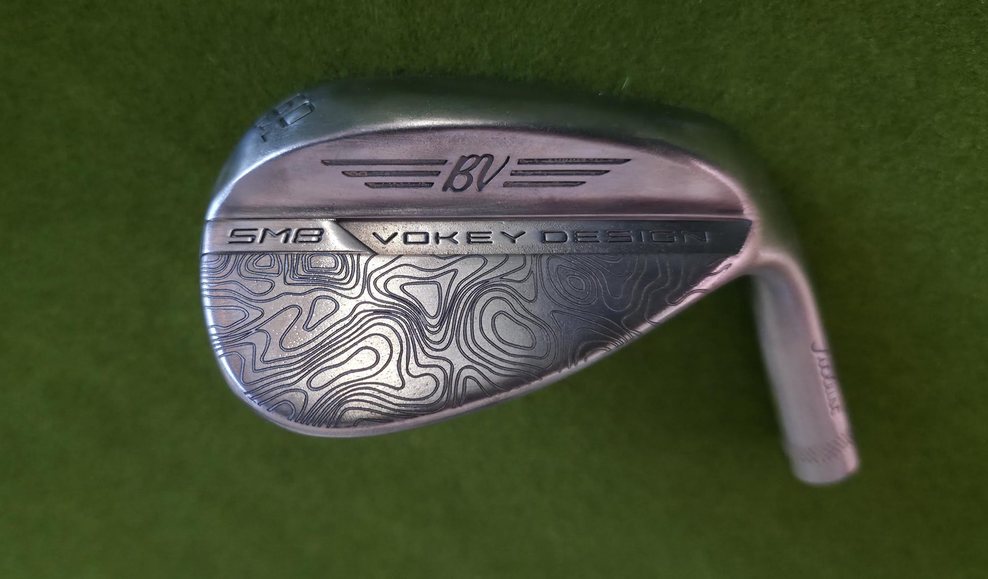 Custom laser-engraved Titleist Vokey SM8 golf wedge by Par Bros Golf, featuring a detailed, wrap-around topographic map pattern. The intricate artisan etching covers the steel clubhead, highlighting unique personalized craftsmanship. Titleist Vokey Design SM8 wedge with deep, intricate topographic map-style laser engraving covering the clubhead's surface. The 'BV' logo, 'SM8', and 'VOKEY DESIGN' markings are clearly visible on the brushed steel finish.