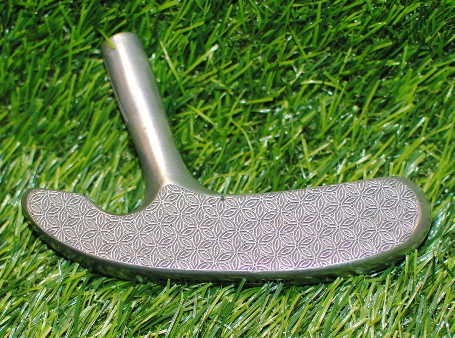May include: A silver-colored golf club putter with a patterned grip. The putter is angled slightly, showcasing its design and the texture of the grip. The club is set against a marble-like surface.