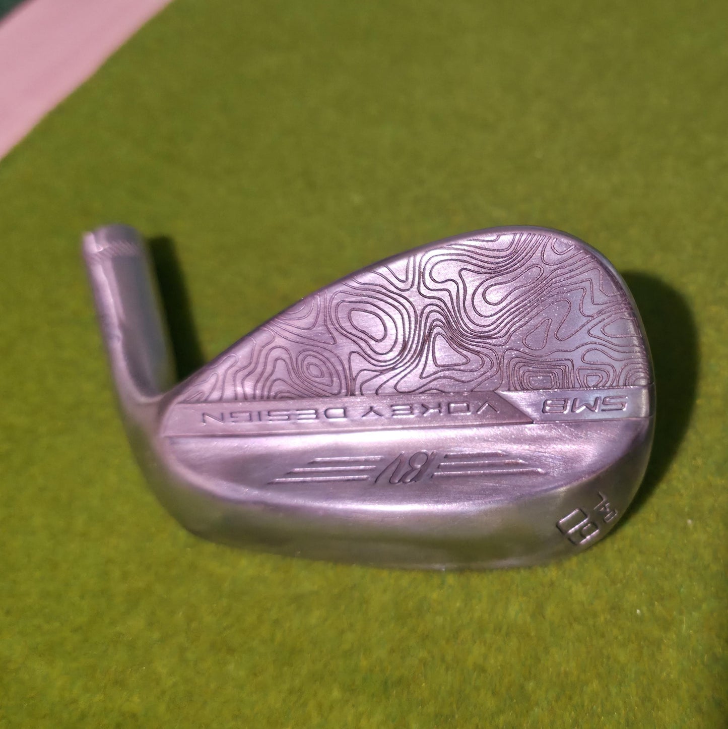 Custom laser-engraved Titleist Vokey SM8 golf wedge by Par Bros Golf, featuring a detailed, wrap-around topographic map pattern. The intricate artisan etching covers the steel clubhead, highlighting unique personalized craftsmanship. Titleist Vokey Design SM8 wedge with deep, intricate topographic map-style laser engraving covering the clubhead's surface. The 'BV' logo, 'SM8', and 'VOKEY DESIGN' markings are clearly visible on the brushed steel finish.