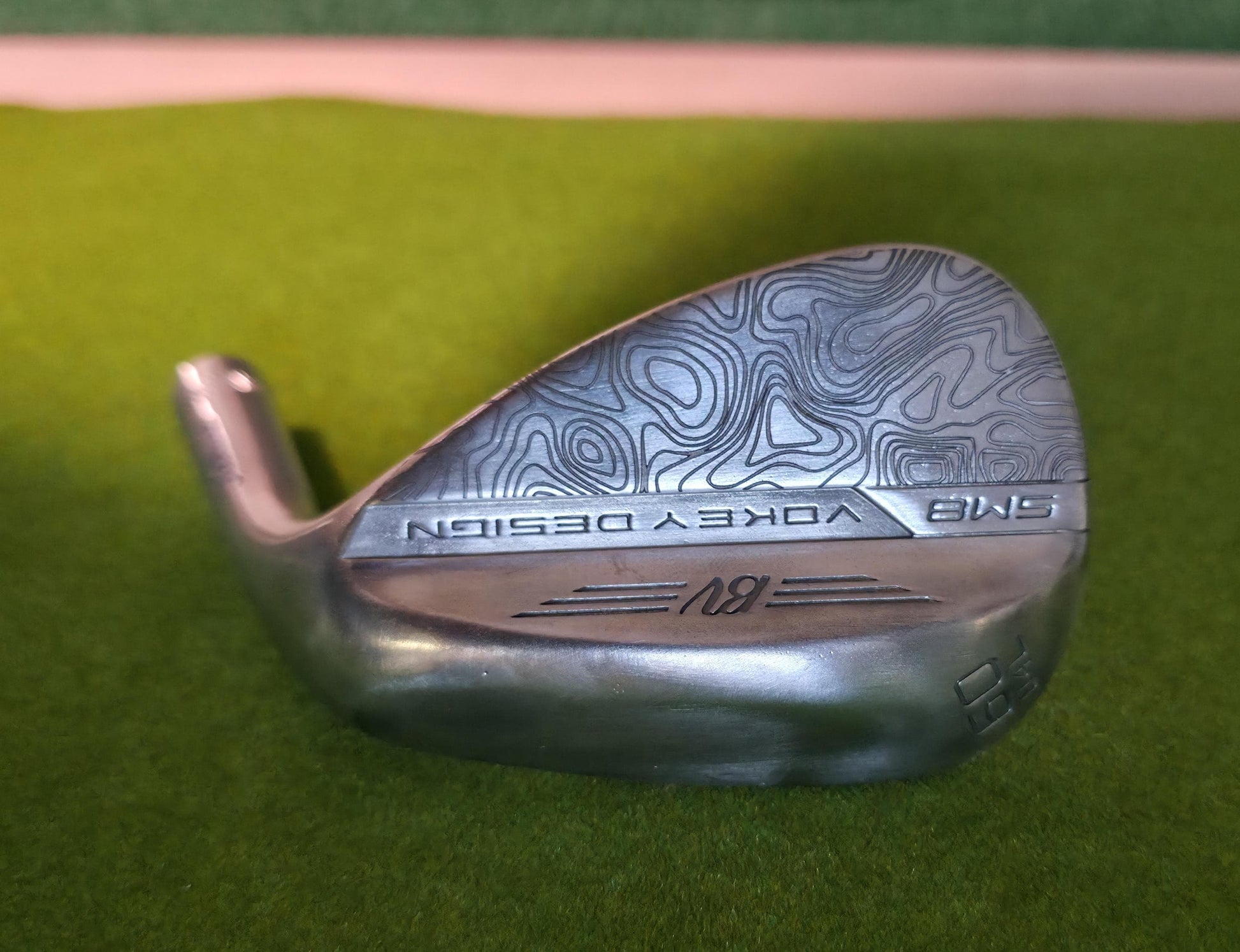 Custom laser-engraved Titleist Vokey SM8 golf wedge by Par Bros Golf, featuring a detailed, wrap-around topographic map pattern. The intricate artisan etching covers the steel clubhead, highlighting unique personalized craftsmanship. Titleist Vokey Design SM8 wedge with deep, intricate topographic map-style laser engraving covering the clubhead's surface. The 'BV' logo, 'SM8', and 'VOKEY DESIGN' markings are clearly visible on the brushed steel finish.