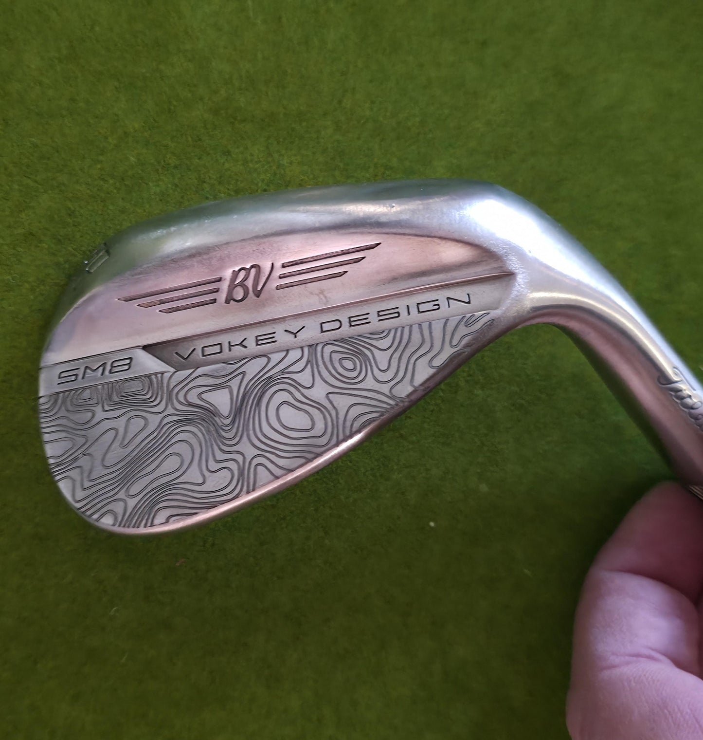 Custom laser-engraved Titleist Vokey SM8 golf wedge by Par Bros Golf, featuring a detailed, wrap-around topographic map pattern. The intricate artisan etching covers the steel clubhead, highlighting unique personalized craftsmanship. Titleist Vokey Design SM8 wedge with deep, intricate topographic map-style laser engraving covering the clubhead's surface. The 'BV' logo, 'SM8', and 'VOKEY DESIGN' markings are clearly visible on the brushed steel finish.