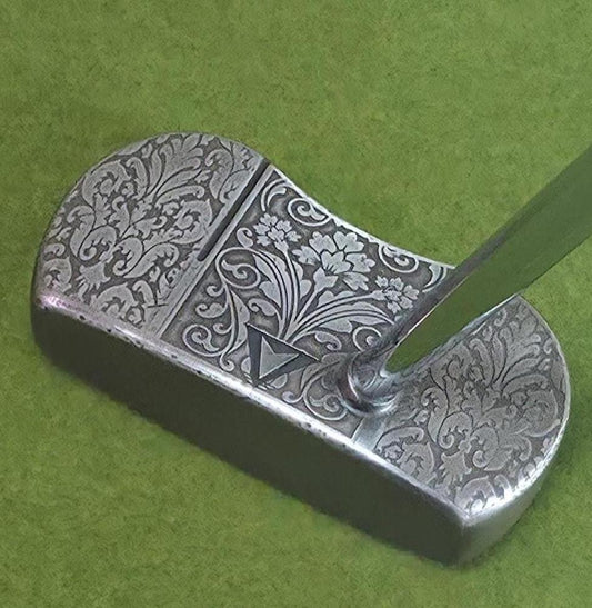 Custom engraved golf putter head with ornate floral and scrollwork design in antique brushed metal finish. Features deep engraving for durability, luxury artisan detailing, and an elegant symmetrical pattern. Perfect for golfers seeking a unique club, golf collectors, or as a personalized gift with initials, logos, or dates added. A blend of performance and craftsmanship designed to stand out on the green or in a golf display collection