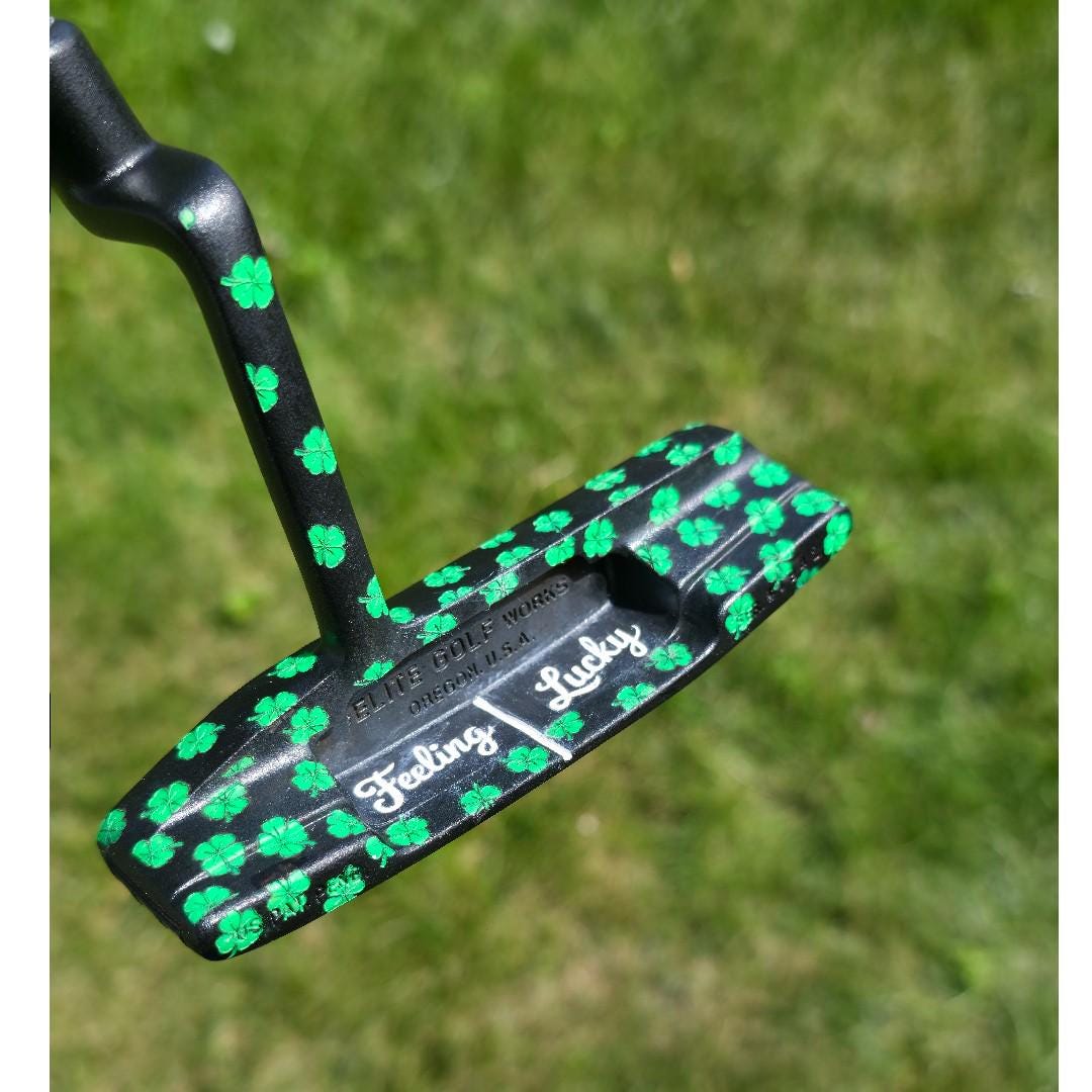 Custom black golf putter with green shamrock clover pattern, "Feeling Lucky" engraving, white alignment line, and Elite Golf Works USA branding — novelty St. Patrick’s Day golf gift for Irish golf lovers and collectors  custom golf putter  black putter head  green shamrock / clover pattern  “Feeling Lucky” engraving  alignment line  Elite Golf Works USA  St. Patrick’s Day golf gift  novelty golf club  Irish golf lovers  collectors