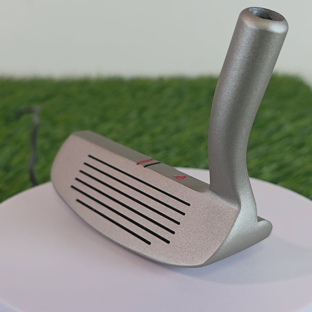 Silver golf chipper on green turf. Back features black and red laser-engraved street art silhouettes: a girl reaching for a red heart balloon, and a man throwing red flowers. Top line has a red heart and black/red alignment stripes. The front face shows standard horizontal scoring lines. The metal club head connects to a silver shaft at the heel. These high-contrast deep engravings are meticulously crafted. Perfect visual representation of custom golf equipment blending modern art with the utility.